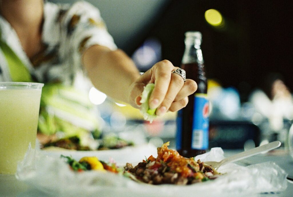 A person squeezes lime on tacos with refreshing beverage at a bustling street food market in Guadalajara.